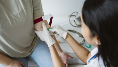 High angle view of doctor piercing needle in patient's arm for medical exam in clinic