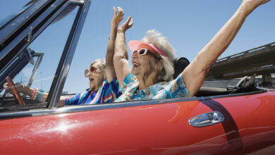 Two senior women in convertible car, arms outstretched, side view