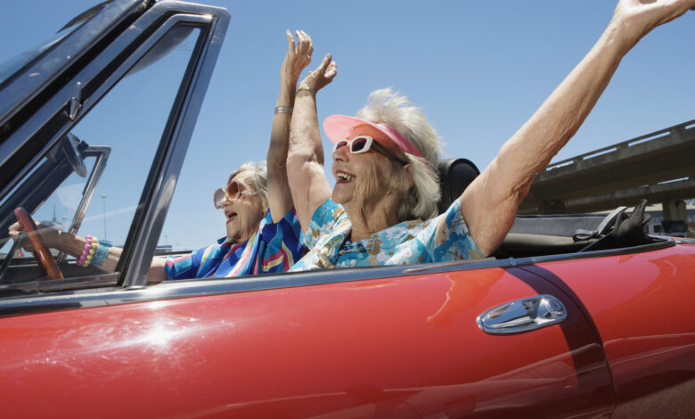 Two senior women in convertible car, arms outstretched, side view