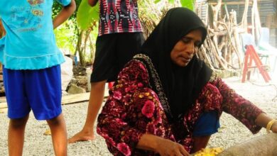 A mother is using traditional Maldivian cooking utensils to prepare a meal for her children.