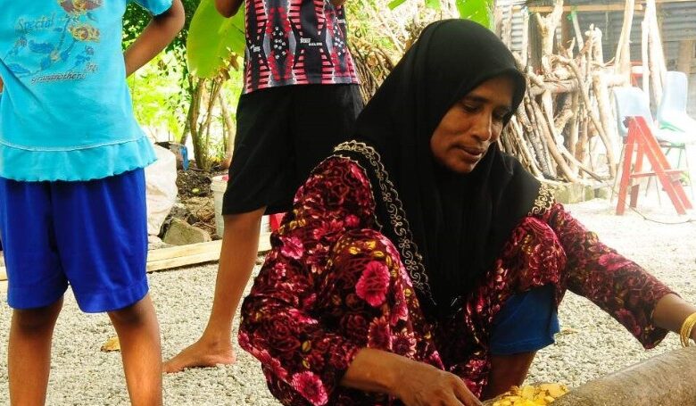 A mother is using traditional Maldivian cooking utensils to prepare a meal for her children.