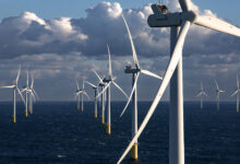 Offshore wind turbines stand tall above the ocean with a cloudy blue sky in the background