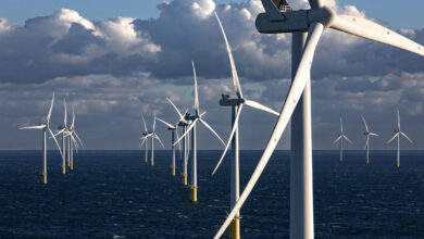 Offshore wind turbines stand tall above the ocean with a cloudy blue sky in the background