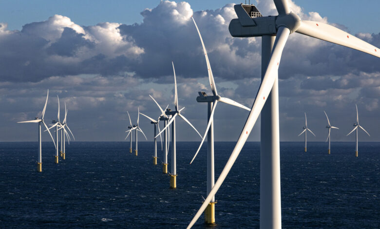 Offshore wind turbines stand tall above the ocean with a cloudy blue sky in the background