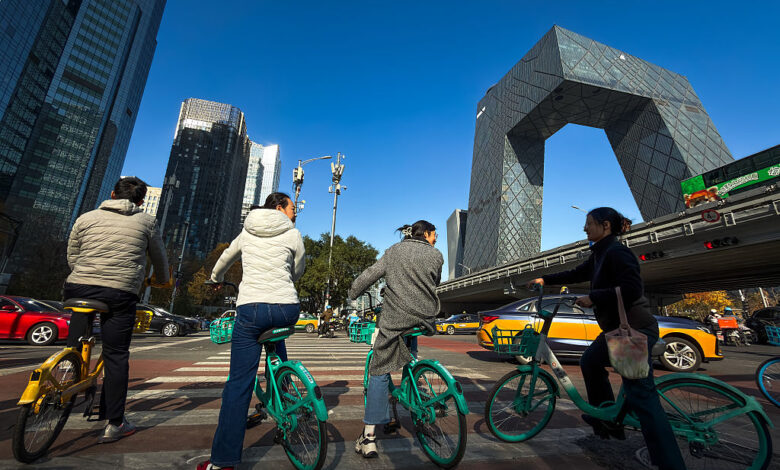 Cyclists Wait At An Intersection Near The CCTV Headquarters In Beijing