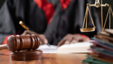 Focus on judge gavel, Unrecognizable judge busy writing verdict or making notes from the book with gavel and balance scale on table.