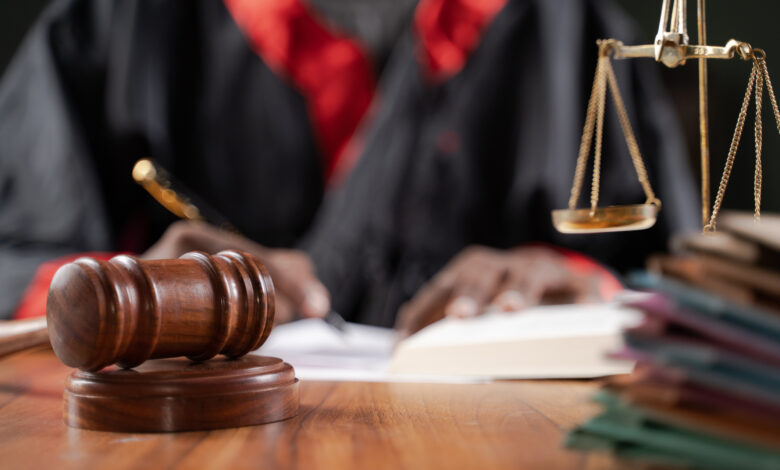 Focus on judge gavel, Unrecognizable judge busy writing verdict or making notes from the book with gavel and balance scale on table.