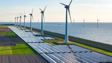 Drone point of view of wind turbines and solar panel fields situated along a coastline