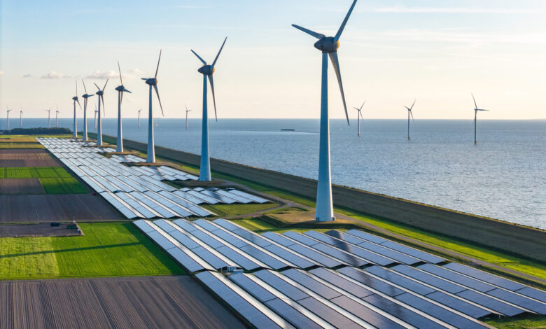 Drone point of view of wind turbines and solar panel fields situated along a coastline