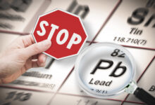 Stop heavy metals - Concept image with hand holding a stop sign against a Lead chemical element with the Mendeleev periodic table seen through a magnifying glass