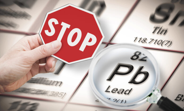 Stop heavy metals - Concept image with hand holding a stop sign against a Lead chemical element with the Mendeleev periodic table seen through a magnifying glass