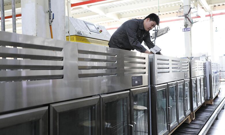 worker injecting refrigerant into freezers on a production line at a kitchen utensils manufacturer in Binzhou, Shandong province.